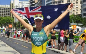 Australian Paralympian Kate Doughty standing with her arms outstretched above her head holding the Australian flag