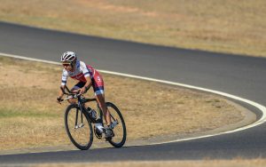 Image of a female cyclist riding on the road. She is wearing a predominantly red and white cycling suit