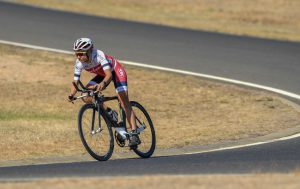 Image of a female cyclist riding on the road. She is wearing a predominantly red and white cycling suit