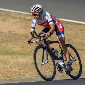 Image of a female cyclist riding on the road. She is wearing a predominantly red and white cycling suit