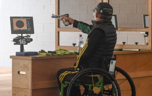 Image of Australian Paralympian Chris Pitt, seated in his wheelchair with his back to the camera, aiming at a target on a shooting range