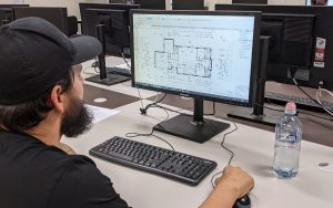 Image of a man sitting in front of computer looking at plans.