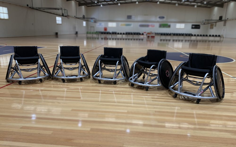 5 empty wheelchairs in a row on an indoor basketball court