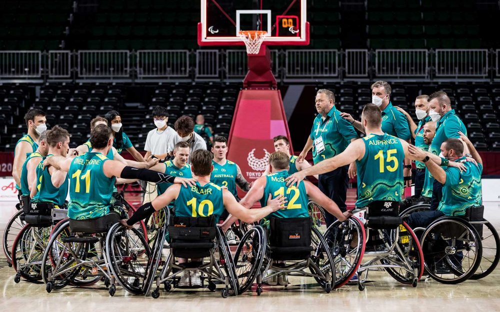 A group wheelchair athletes form a huddle at the end of a basketball game