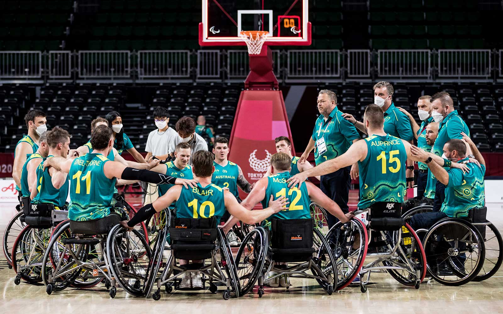 A group wheelchair athletes form a huddle at the end of a basketball game