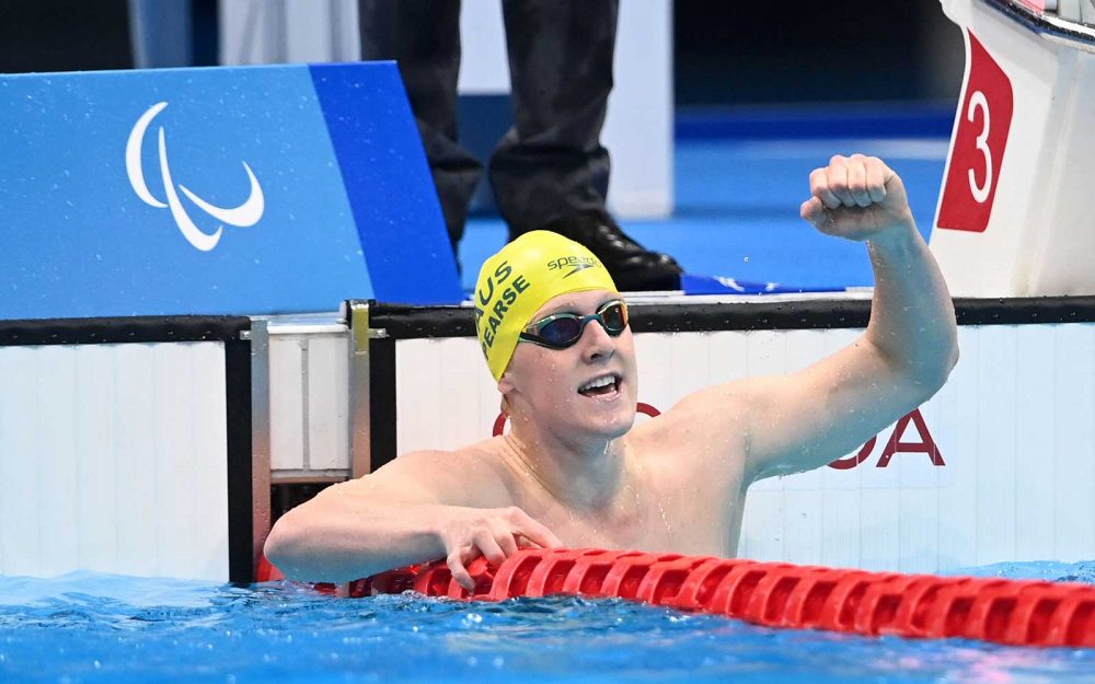 a male swimmer at the end of the race, looks towards the scoreboard and pumps his left fist