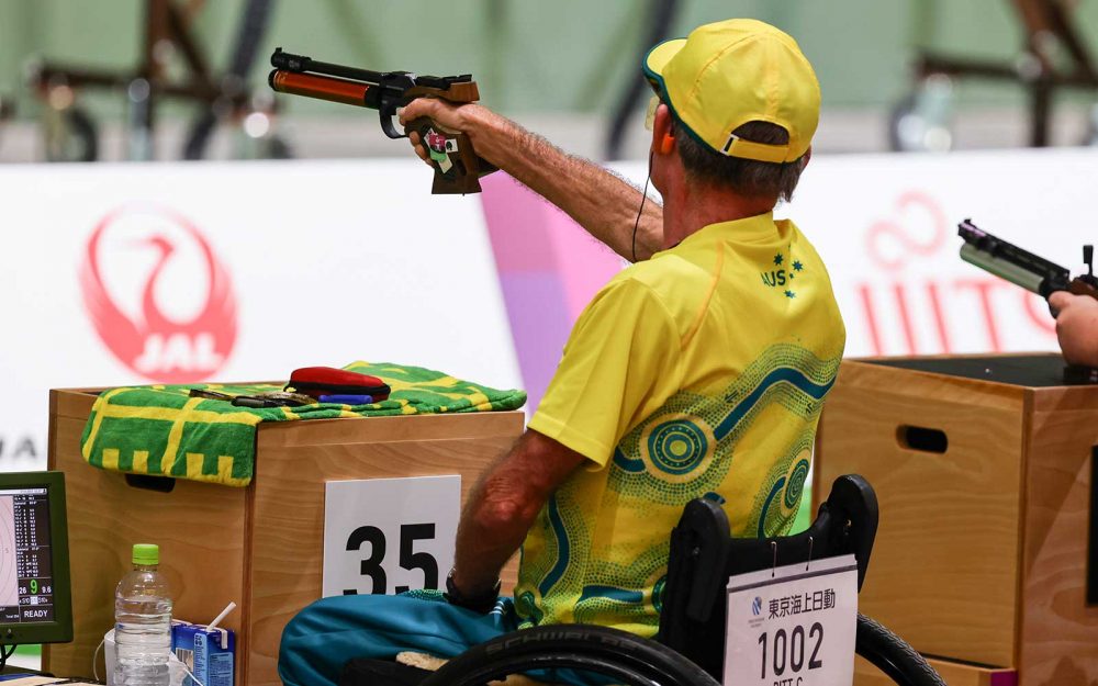 A male representing Australia in a shooting competition. He is aiming at a target