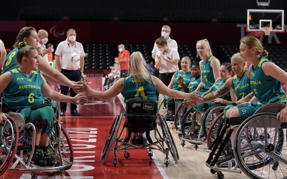 Female wheelchair athletes create a guard of honour for one team-mate. They are high fiving.