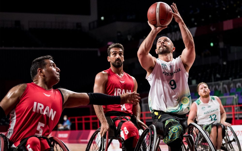 Male Australian Wheelchair Basketball player Tristan Knowles shooting a basketball. He is being defended by a player from Iran.