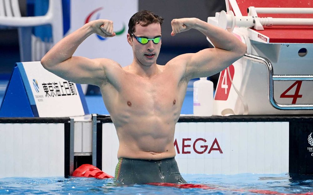 A male swimmer celebrates at the end of a race with arms raised and fists clenched in a muscle pose.
