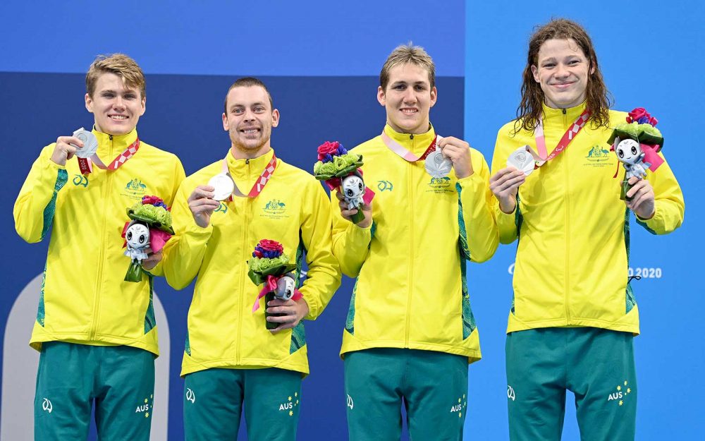 4 Australian male swimmers in green and gold tracksuits stand on the dais with silver medals