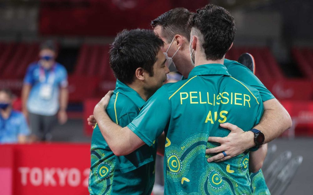 3 members of the Australian men’s table tennis team have a group hug at the end of the match