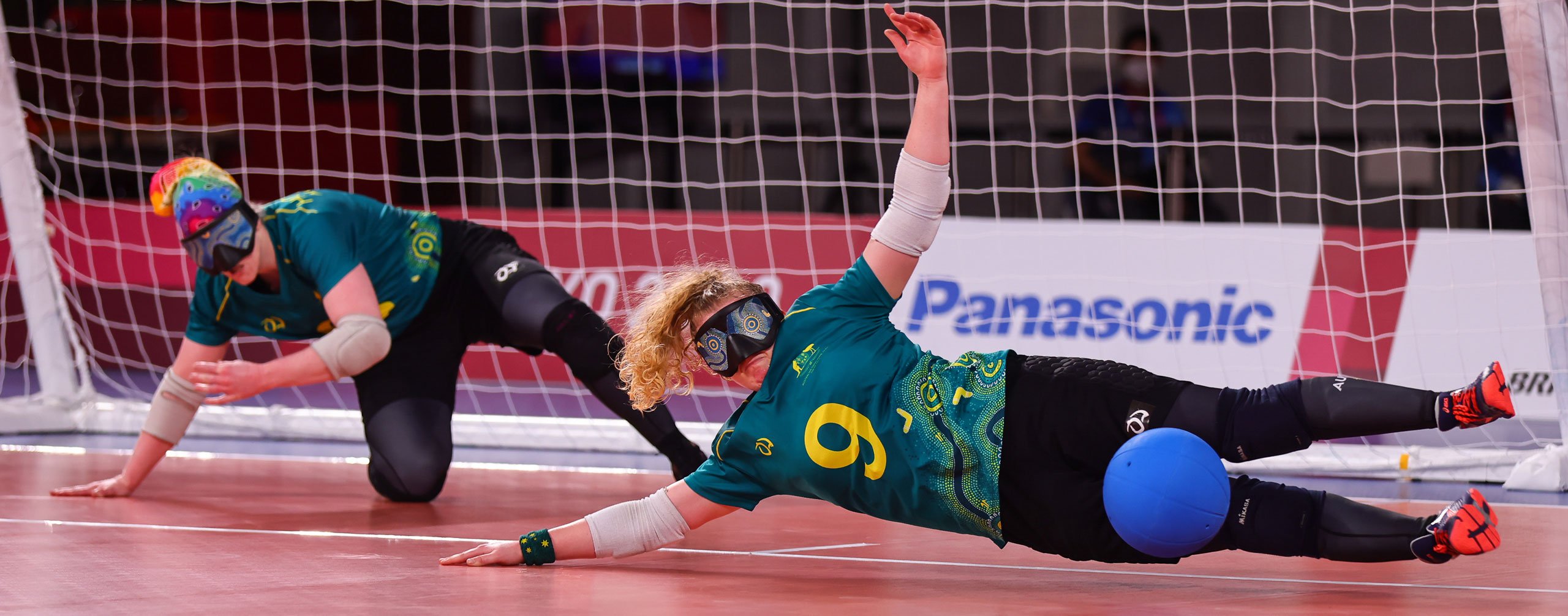 A female Australian Goalball player diving to the left of the image to block a goal