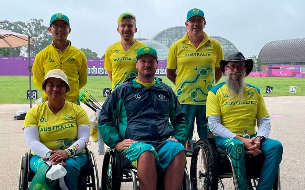 3 people sitting in wheelchairs and 3 people standing behind them. They are wearing Australian Tokyo 2020 uniforms and smiling.