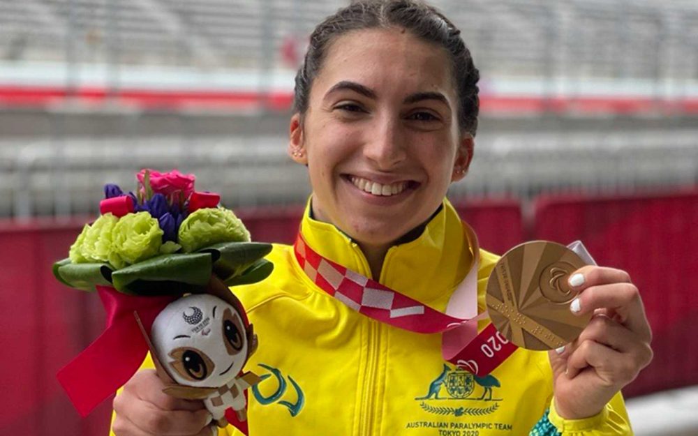 Australian Paralympian Paige Greco is holding a bronze medal in her left hand and smiling at the camera
