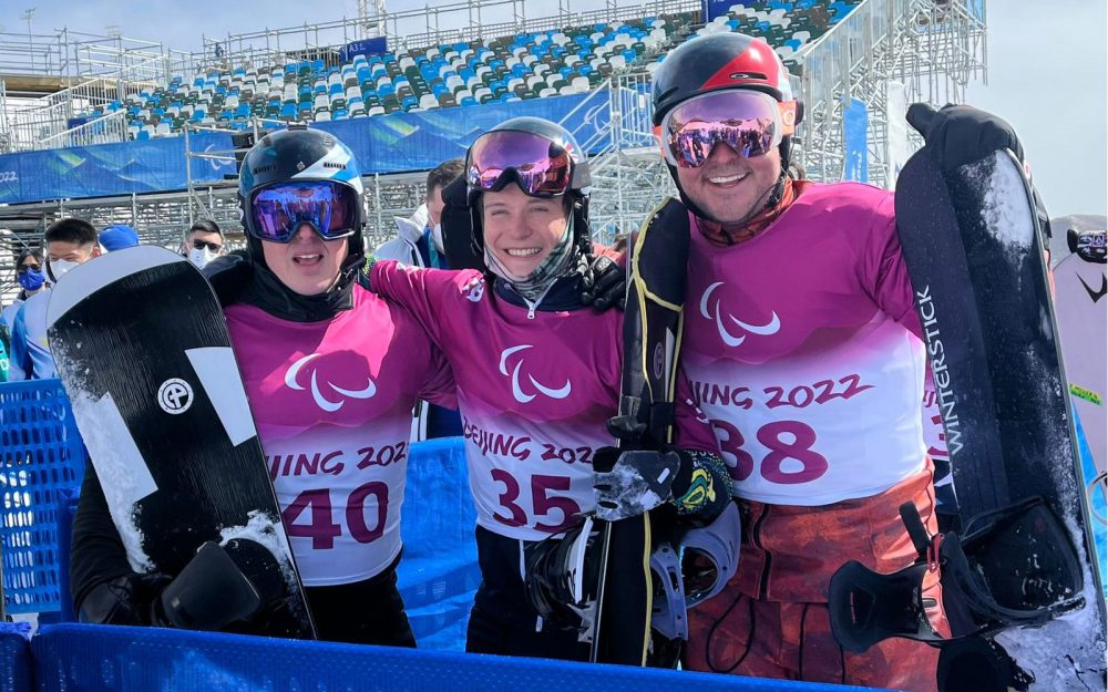 3 male snowboarders in a group smiling at the camera