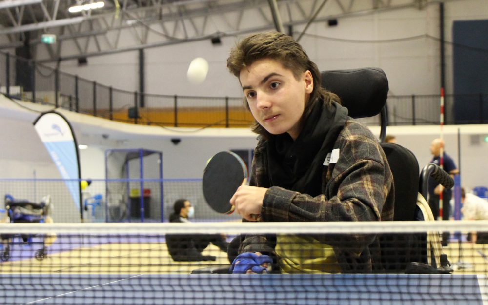 A young person in a wheelchair is playing table tennis