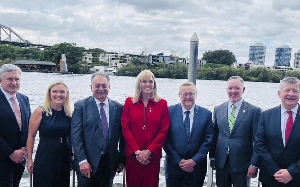 7 business people standing in a line smiling with a river as the backdrop