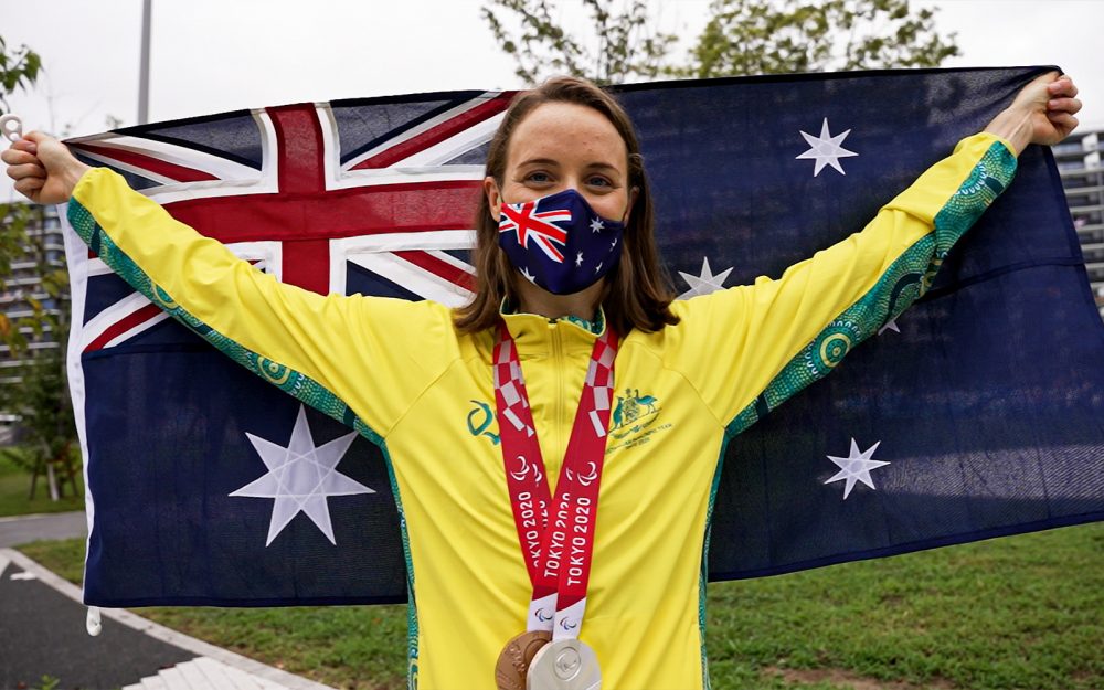Australian Paralympian Ellie Cole holding the Australian flag behind her back. She is wearing an Australian flag facemask and has medal around her neck.