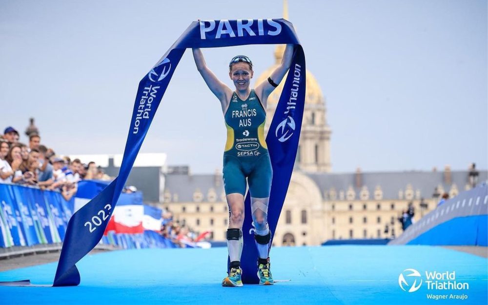 Australian Para-triathlon athlete Anu Francis crossing a finishing line and holding the ribbon above her head in celebration.