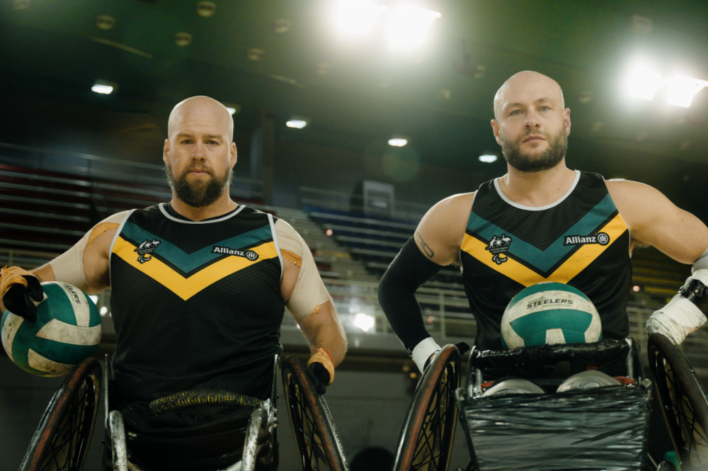 Wheelchair rugby stars Ryley Batt and Chris Bond pose i n their wheelchairs, each holding a ball.