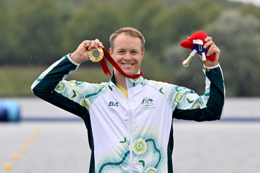 Curtis McGrath holds his gold medal that is draped around his neck.