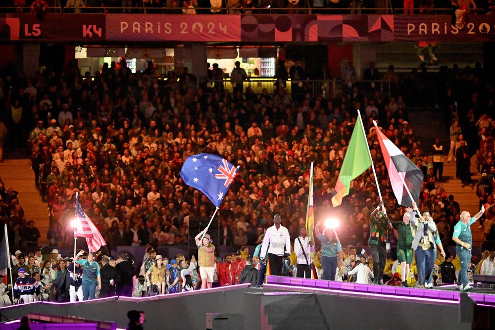 Lauren Parker and James Turner carry the flag in the closing ceremony on stage with flag bearers from other nations.