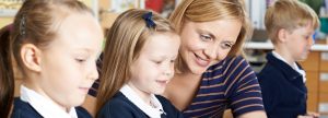 Female teacher in the classroom with two young, female students looking at a book